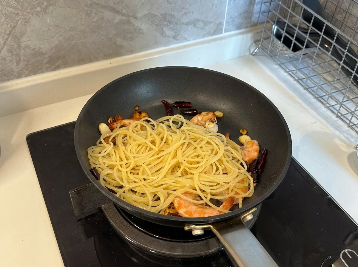 Spaghetti cotti che vengono aggiunti a una padella contenente gamberi, aglio e peperoncino.