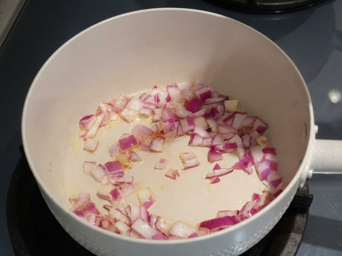 Cipolle rosse tritate che appassiscono in olio in una padella chiara.