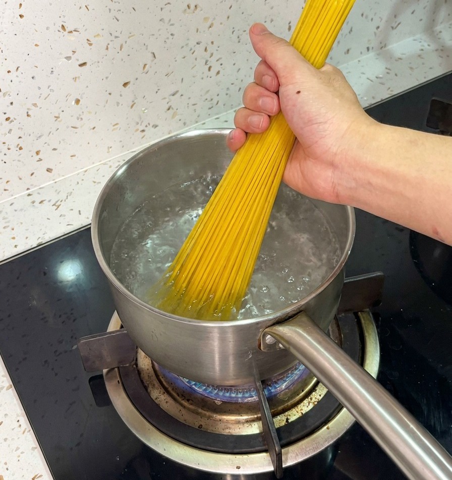 Una mano che immerge un mazzo di spaghetti in una pentola dacciaio con acqua in pieno bollore.