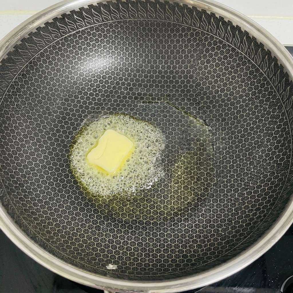 Un panetto di burro giallo che si scioglie e sfrigola al centro di un grande wok scuro.