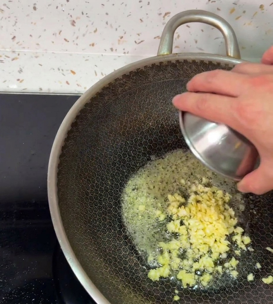 Aglio fresco tritato versato nel burro fuso spumeggiante allinterno di un wok caldo.