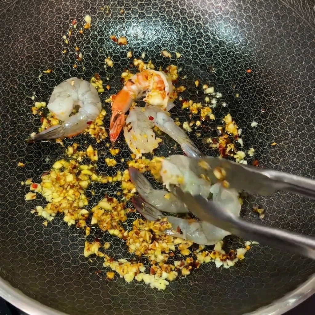 Pinze usate per adagiare i gamberi crudi nel wok condito con burro, aglio e peperoncino.