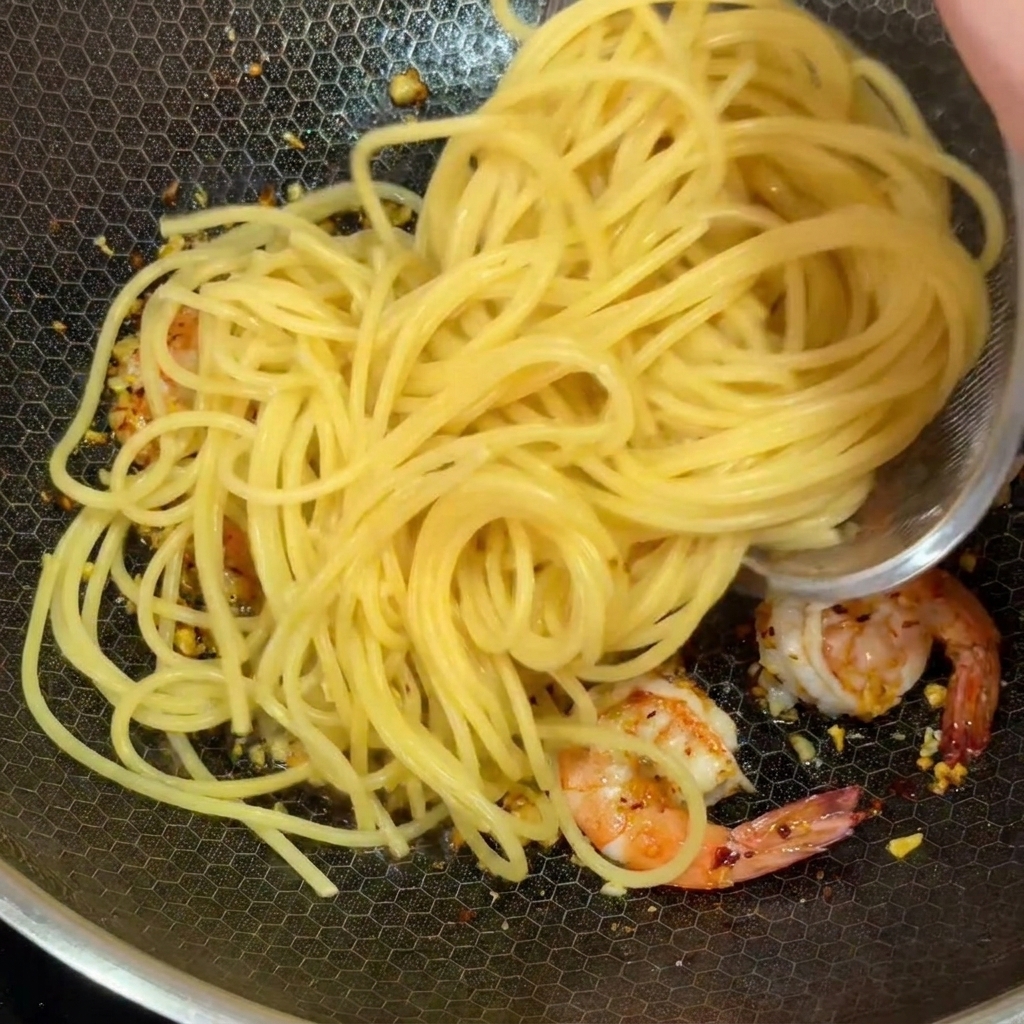 Spaghetti precotti aggiunti nel wok con i gamberi rosa e laglio tritato.