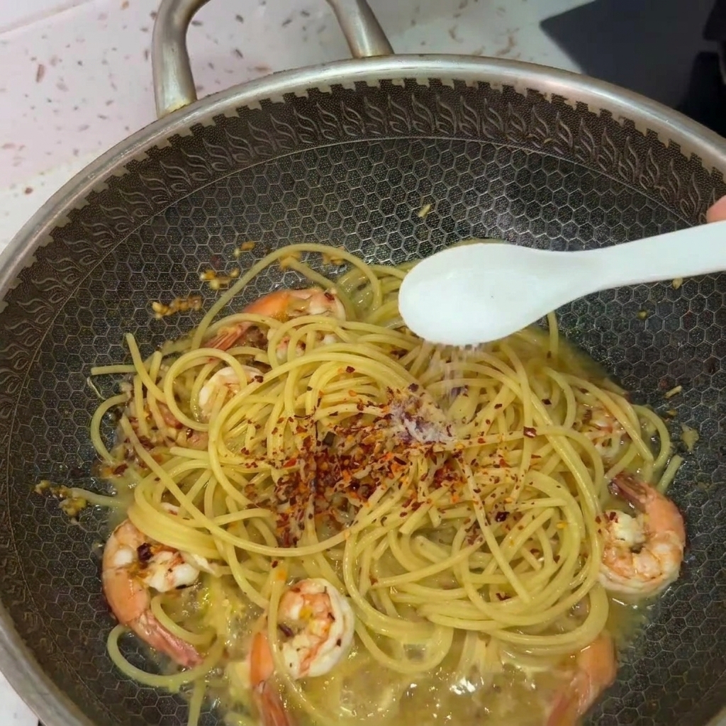 Un cucchiaio che sparge sale sugli spaghetti e i gamberi nel wok guarniti con peperoncino.