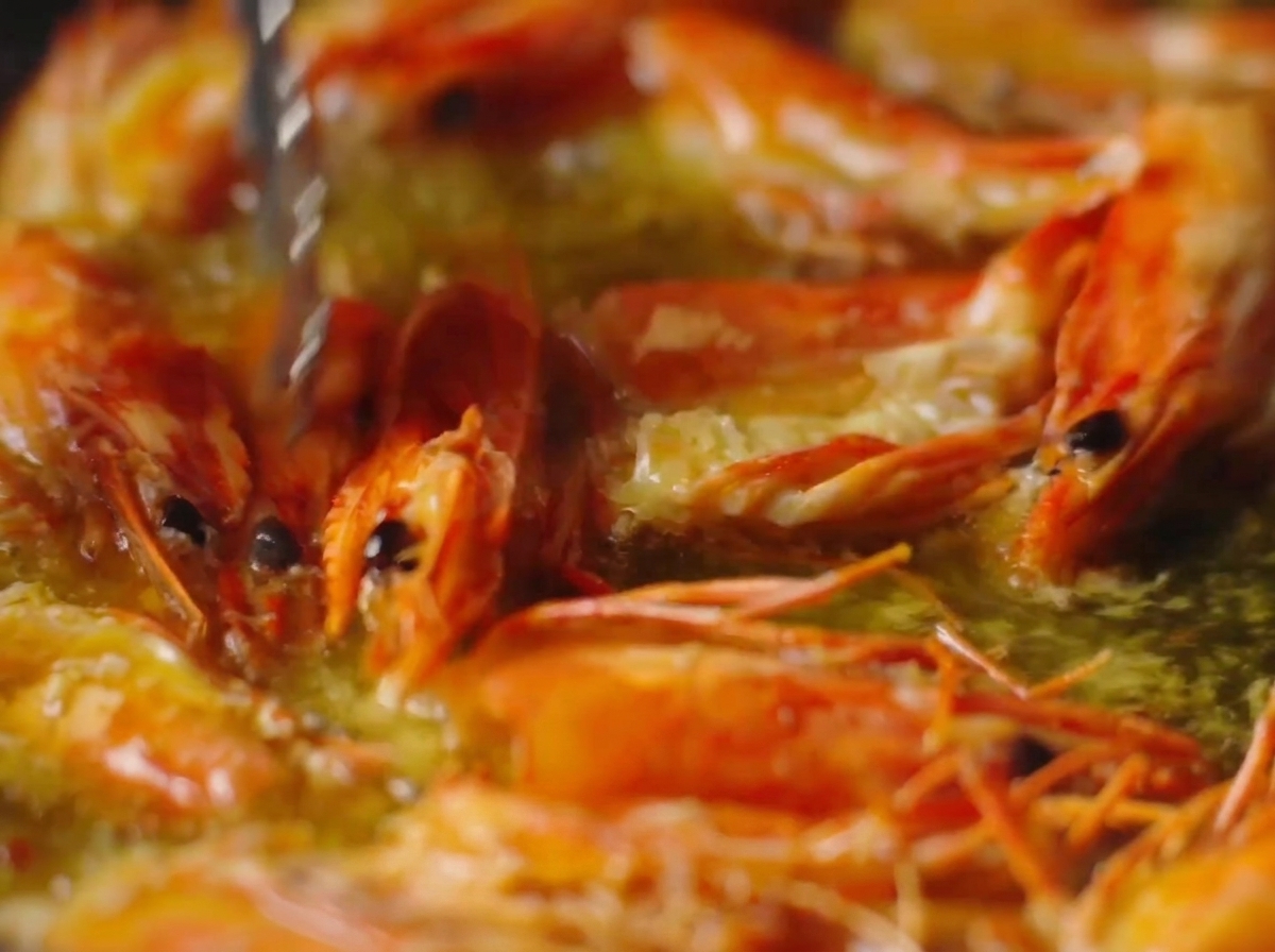 Pinze che premono su teste di gamberi arancioni vibranti che friggono in olio bollente.
