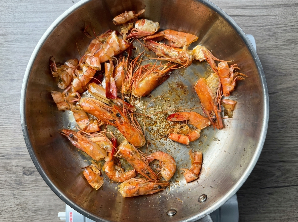 Gusci di gamberi che friggono in olio bollente in una padella dacciaio.