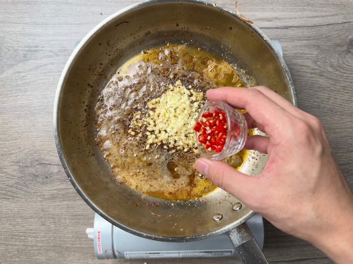 Peperoncino rosso tritato aggiunto a una padella con aglio sfrigolante.