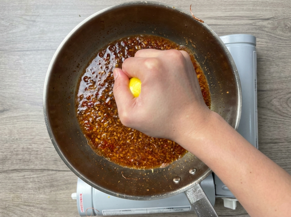 Una mano che spreme mezzo limone fresco in una salsa allaglio gorgogliante in padella.