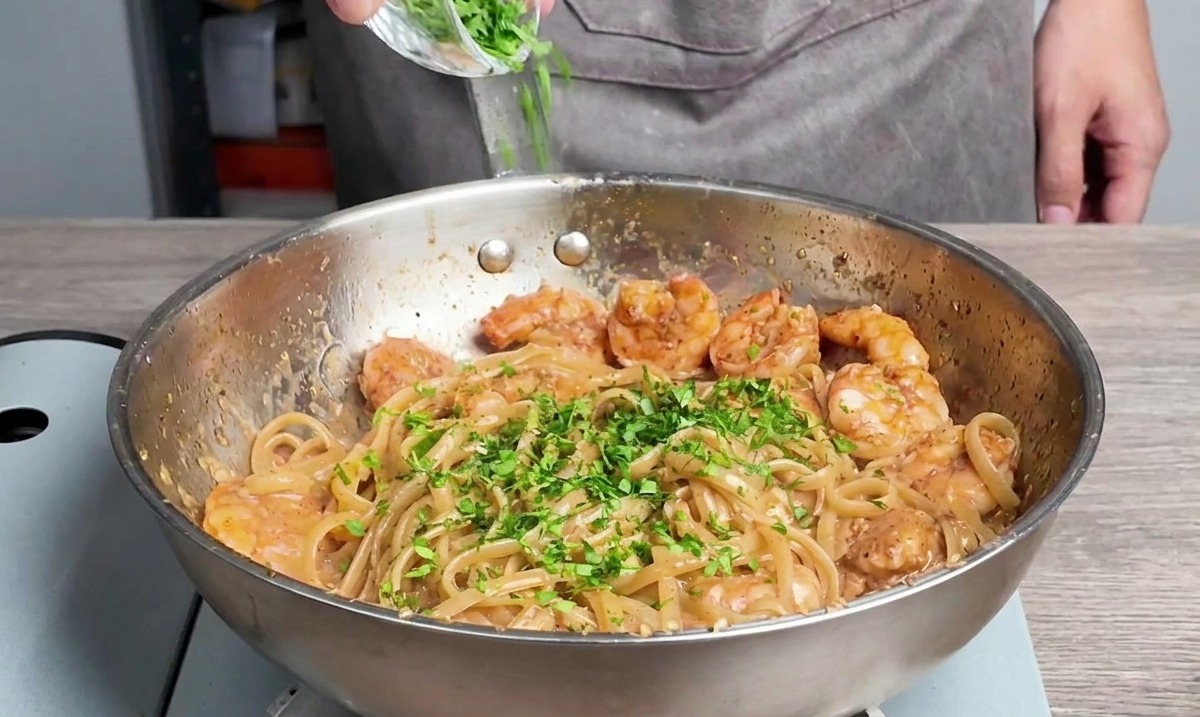 Prezzemolo fresco tritato spolverato sopra linguine e gamberi cotti in padella.