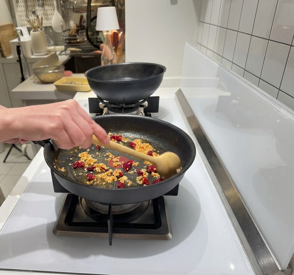 Aglio tritato e peperoncino rosso secco aggiunti a una padella con olio di gamberi sfrigolante dal colore rossastro.