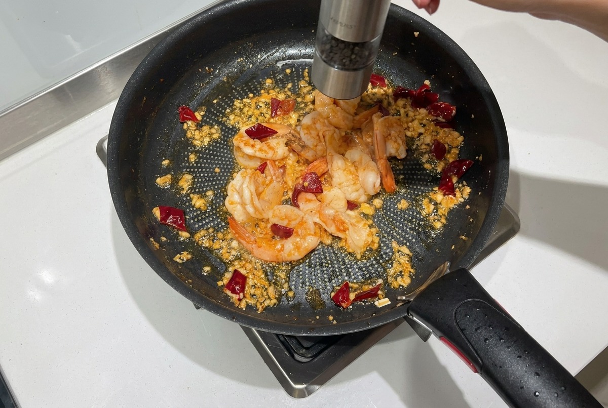 Pepe nero macinato fresco su gamberi rosati parzialmente cotti in una padella.