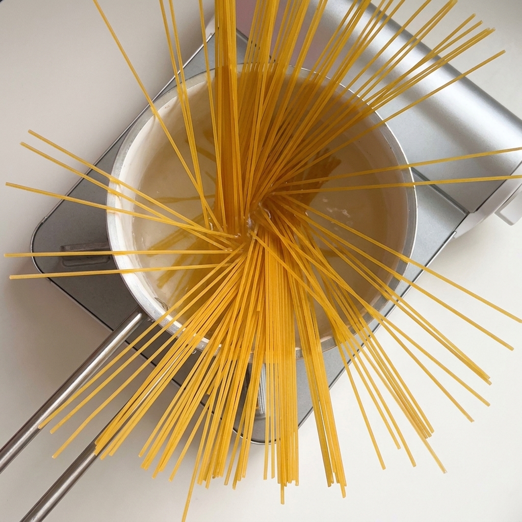 Spaghetti secchi disposti a ventaglio in una pentola di acqua bollente.