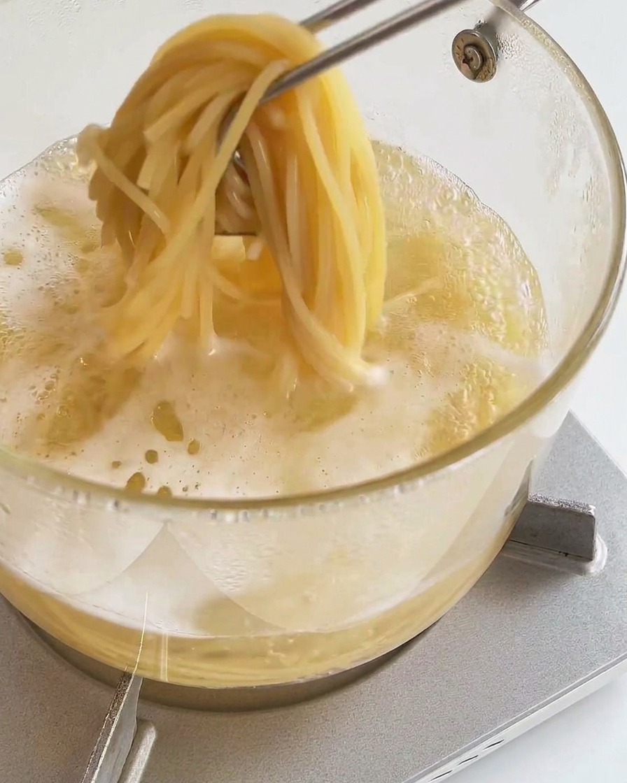 Pinze da cucina che sollevano una porzione di spaghetti cotti dalla pentola.
