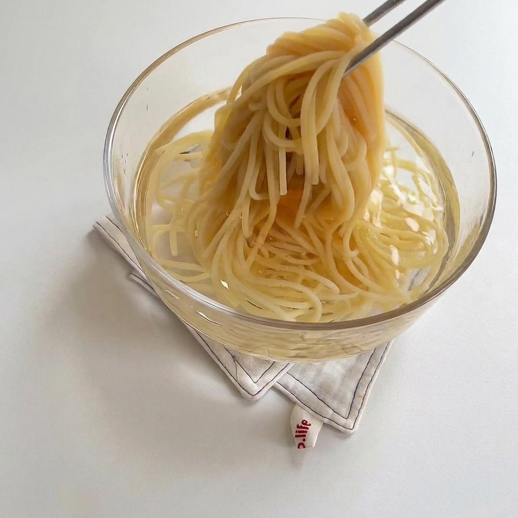 Spaghetti cotti trasferiti in una ciotola di vetro con acqua fredda.