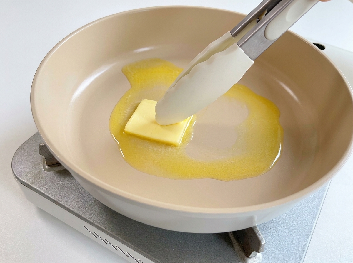 Un cubetto di burro giallo che si scioglie in una padella calda.