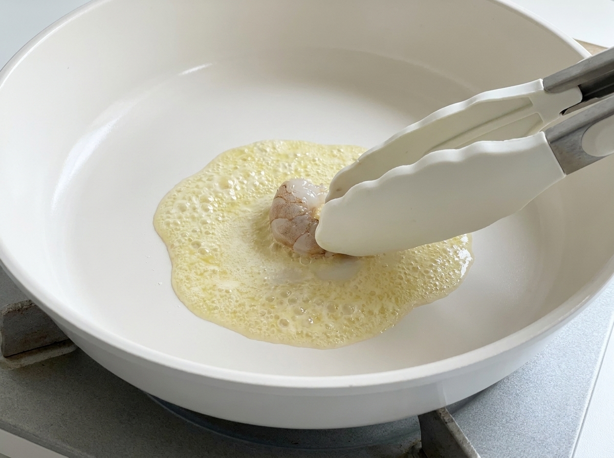 Pinze in silicone che adagiano un gambero crudo nel burro spumeggiante.