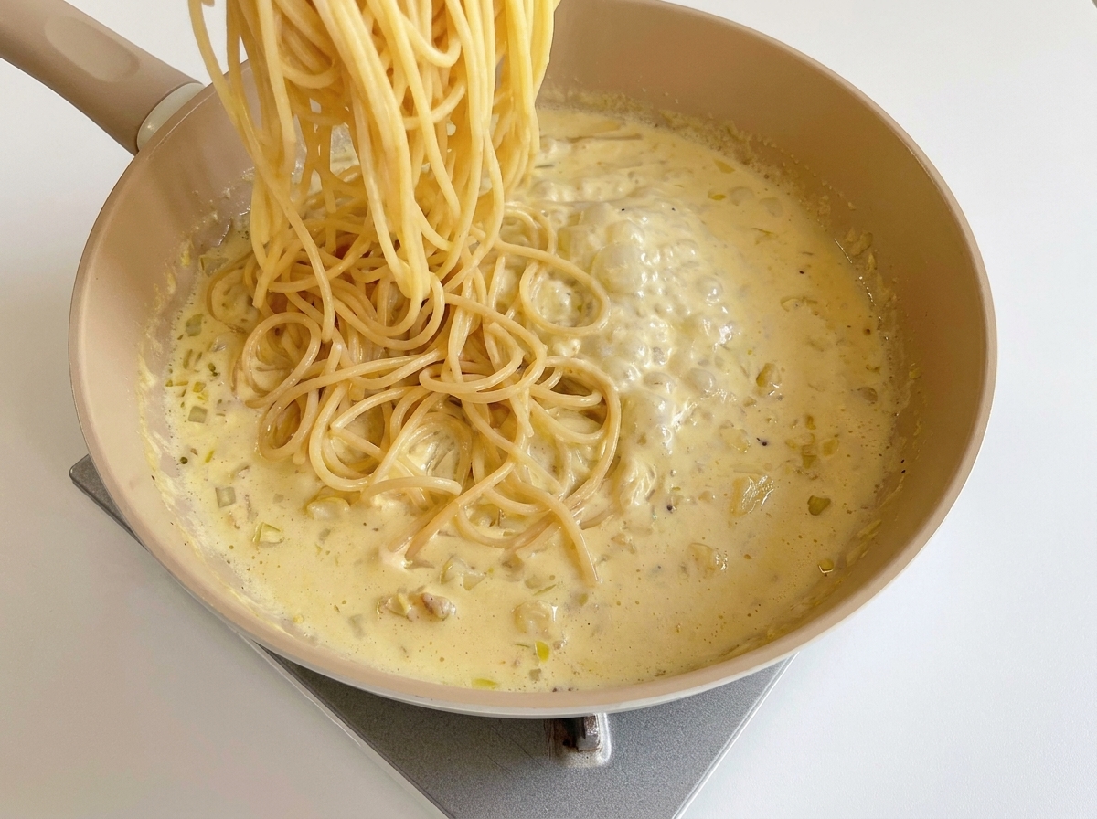 Spaghetti cotti aggiunti alla padella con la salsa cremosa al formaggio.