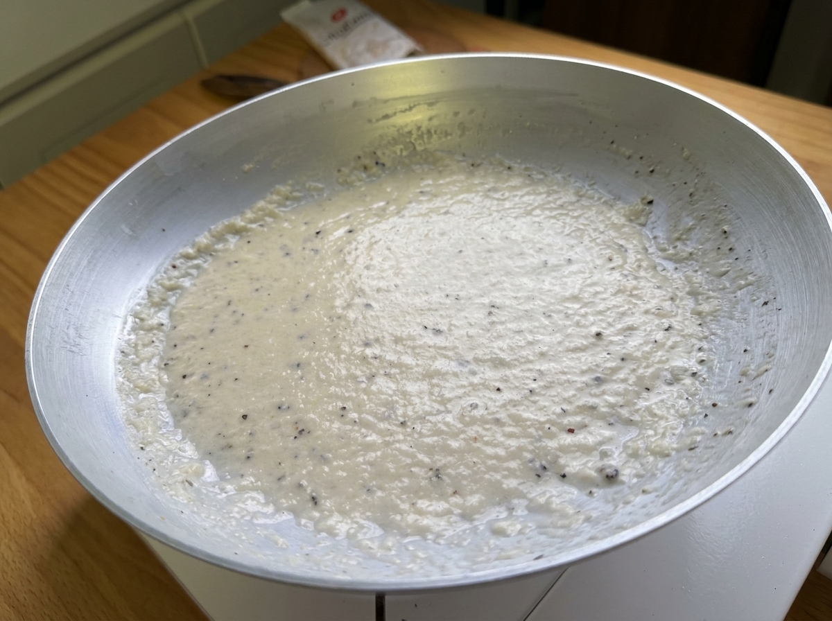 Primo piano di una pasta liscia e cremosa a base di Pecorino e pepe nero adagiata in una padella.