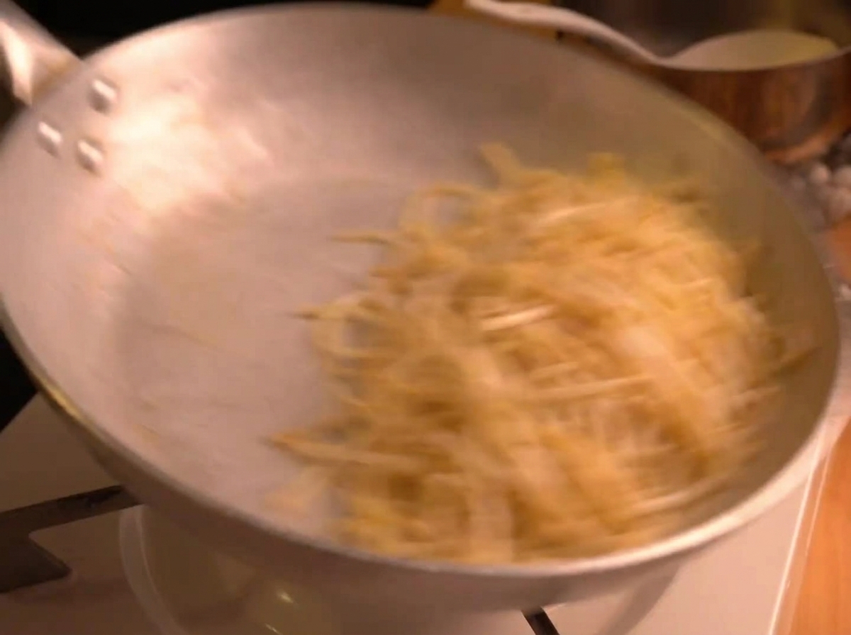 Spaghetti saltati energicamente in una padella dargento, creando un effetto mosso mentre la salsa cremosa si emulsiona.