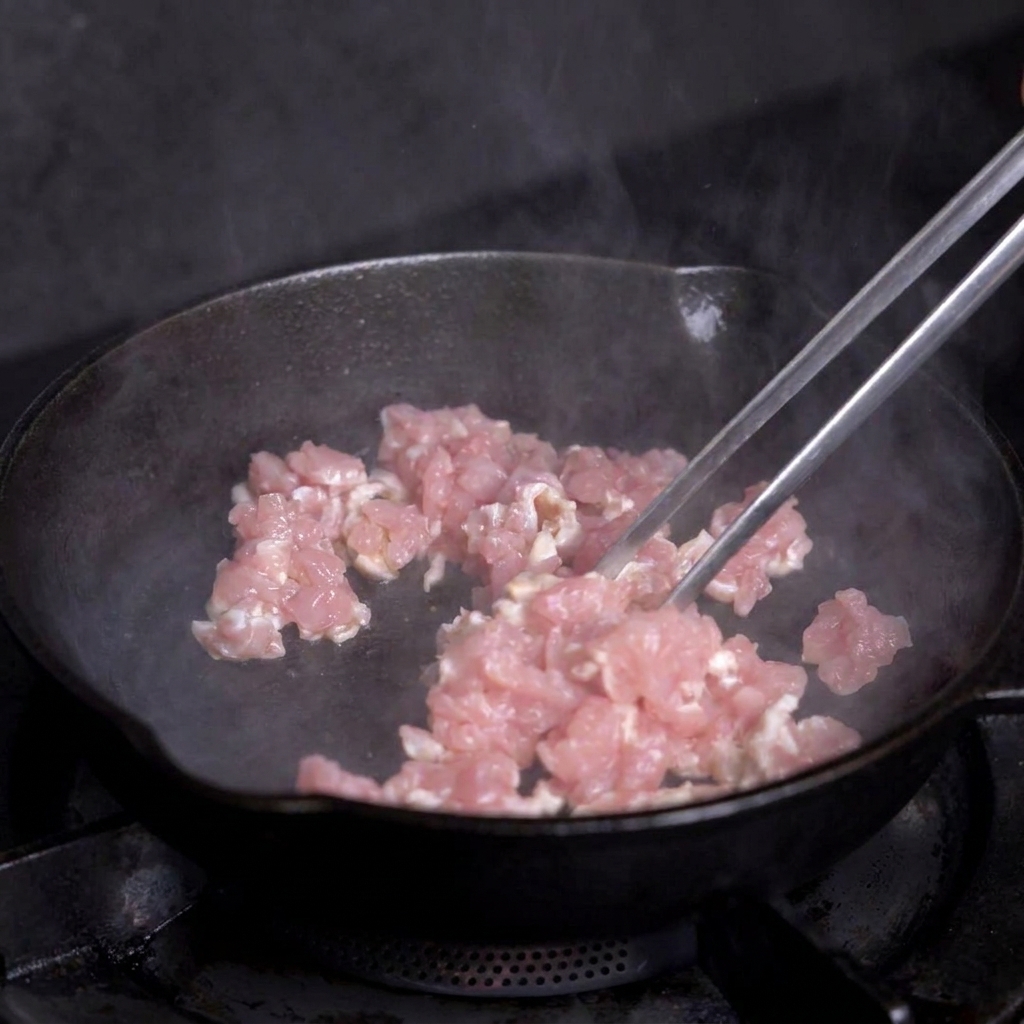 Carne magra a cubetti che cuoce in una padella di ghisa calda mossa con pinze metalliche.