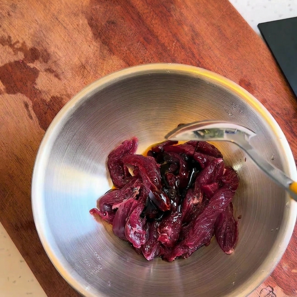 Aggiunta di condimenti liquidi scuri sulle strisce di manzo crudo con un cucchiaio.