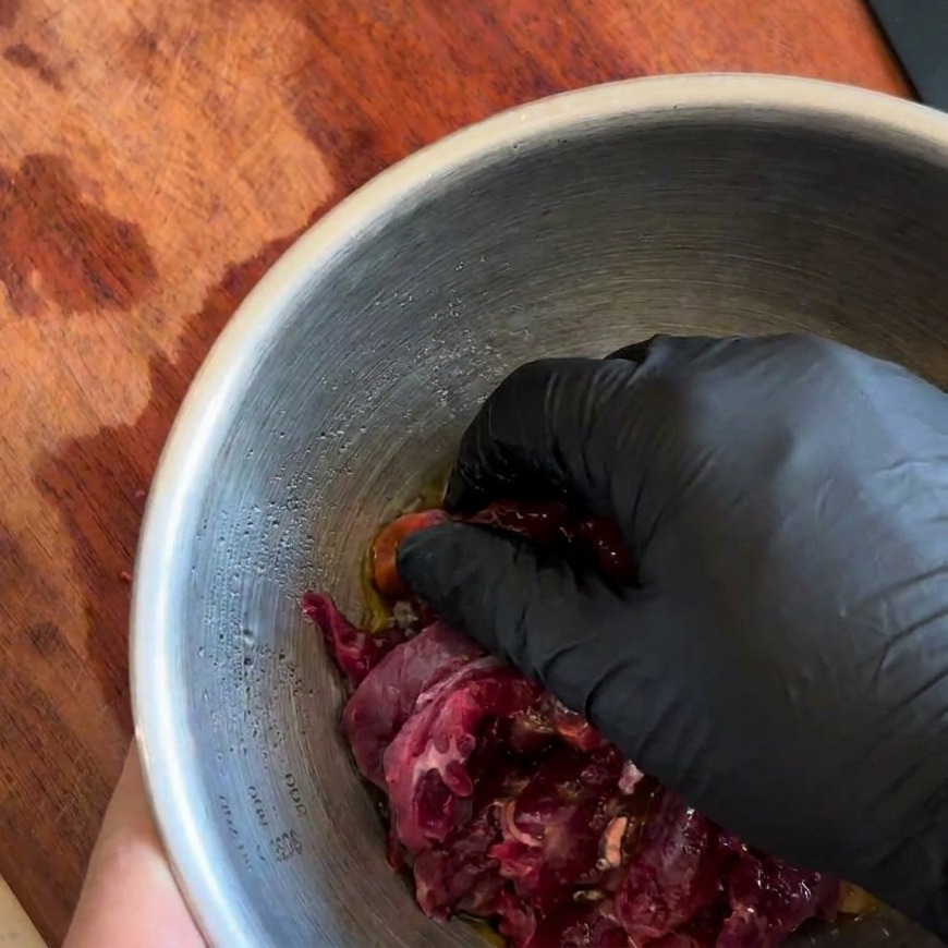 Una mano con guanto che mescola accuratamente il manzo con la marinatura scura.