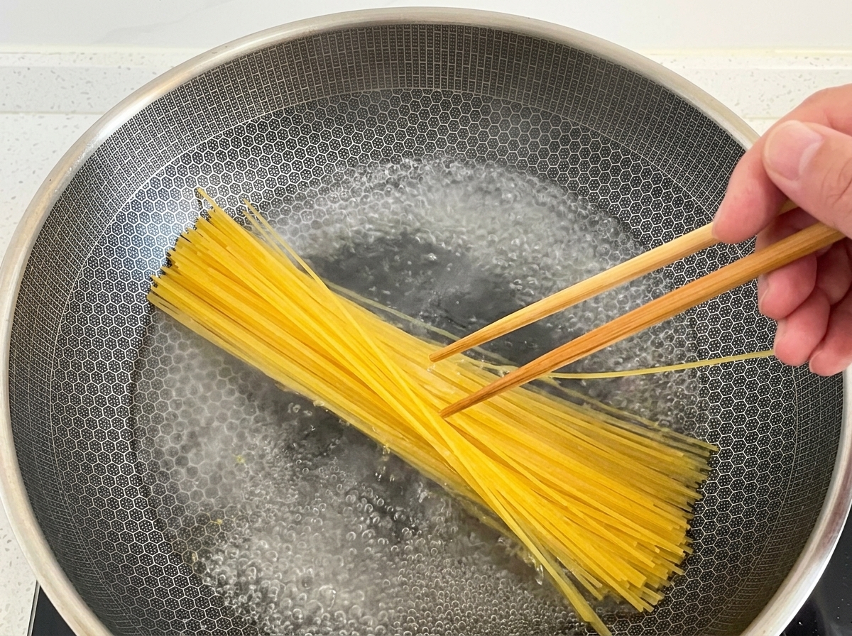 Bacchette di legno che immergono gli spaghetti nellacqua bollente di un wok.