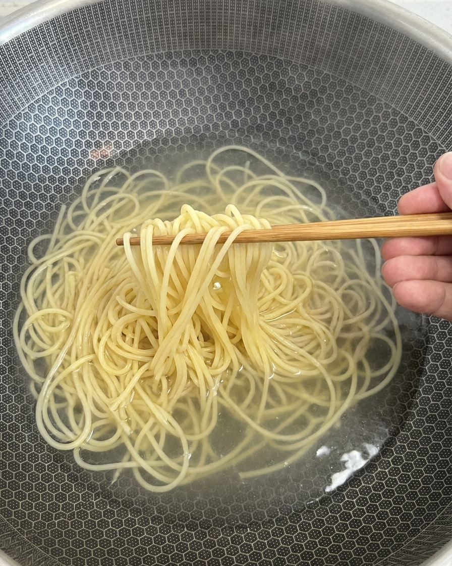 Spaghetti cotti sollevati dallacqua calda con delle bacchette di legno.