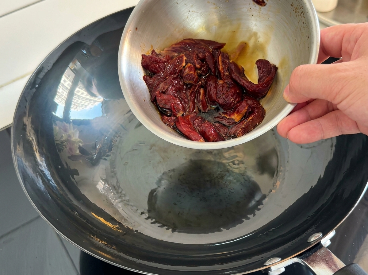 Strisce di manzo marinato versate in un wok rovente con olio.
