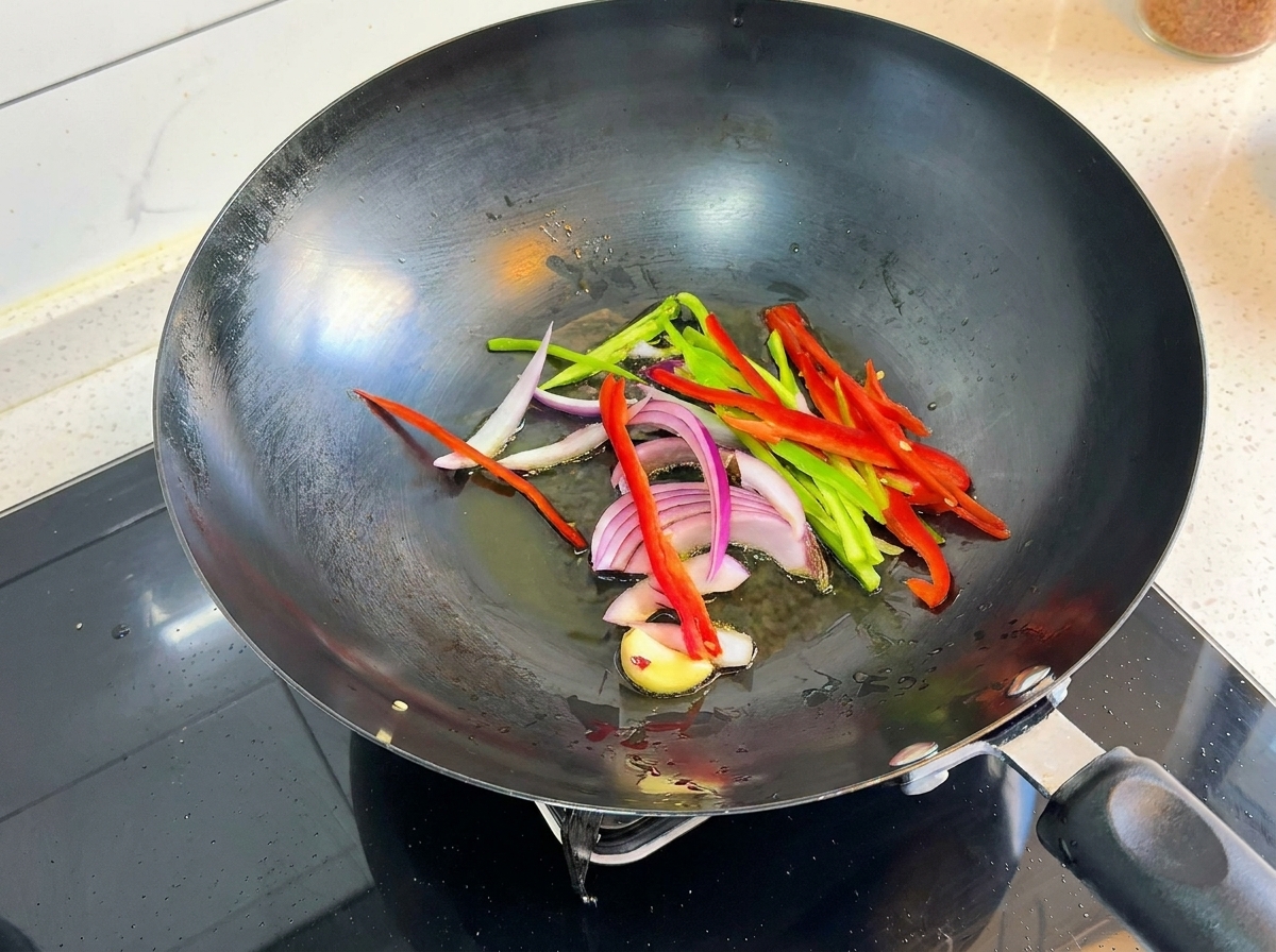 Peperoni, cipolle e aglio che sfrigolano in un wok bollente.