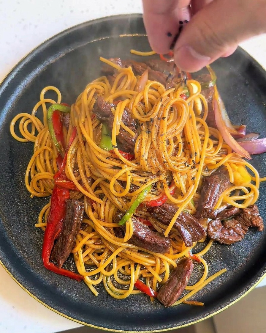Una mano che sparge semi di sesamo nero su un piatto fumante di spaghetti.