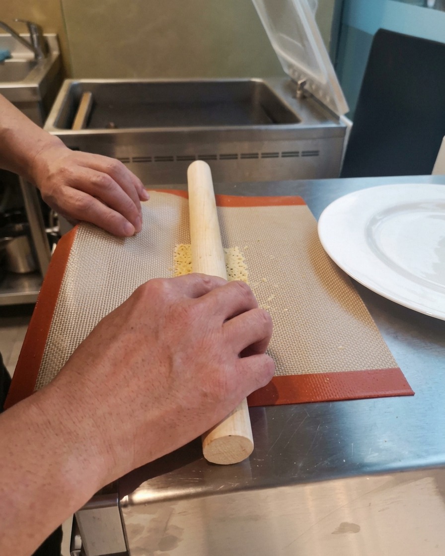 Mani che avvolgono una cialda calda e flessibile attorno a un mattarello di legno su un tappetino in silicone.