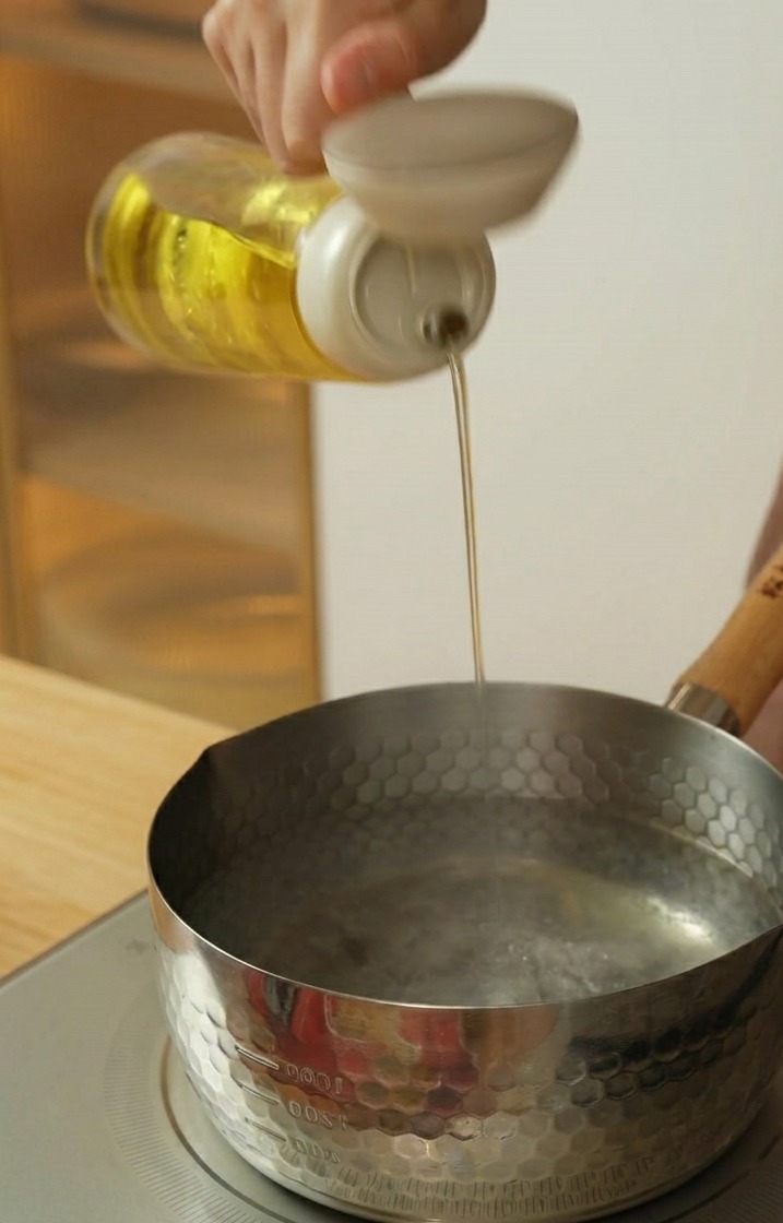 Versare olio di semi in una pentola dacciaio con acqua bollente.