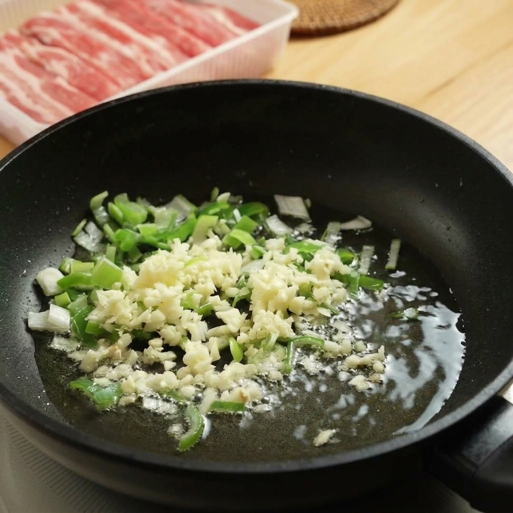 Cipollotto tritato e aglio che sfrigolano in padella con olio caldo.