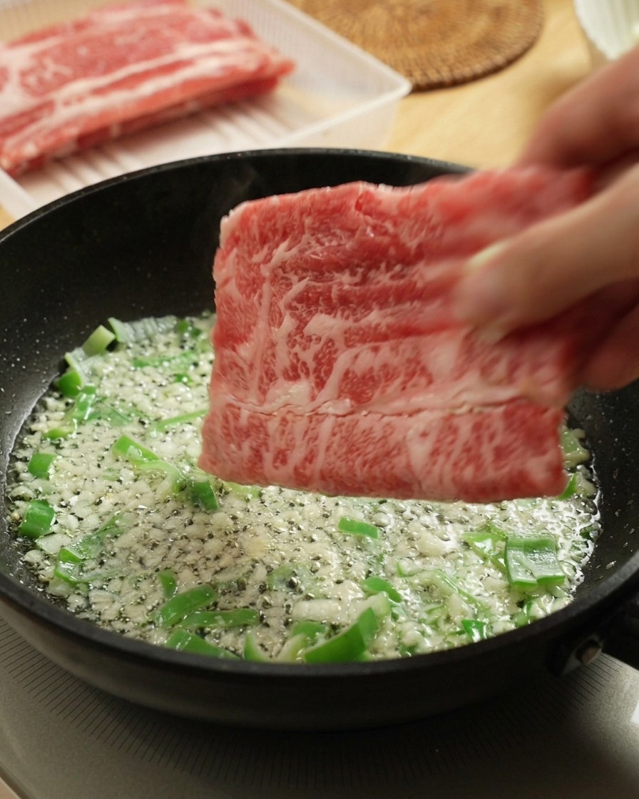 Mettere il manzo crudo a fette in padella con aglio e cipollotti.