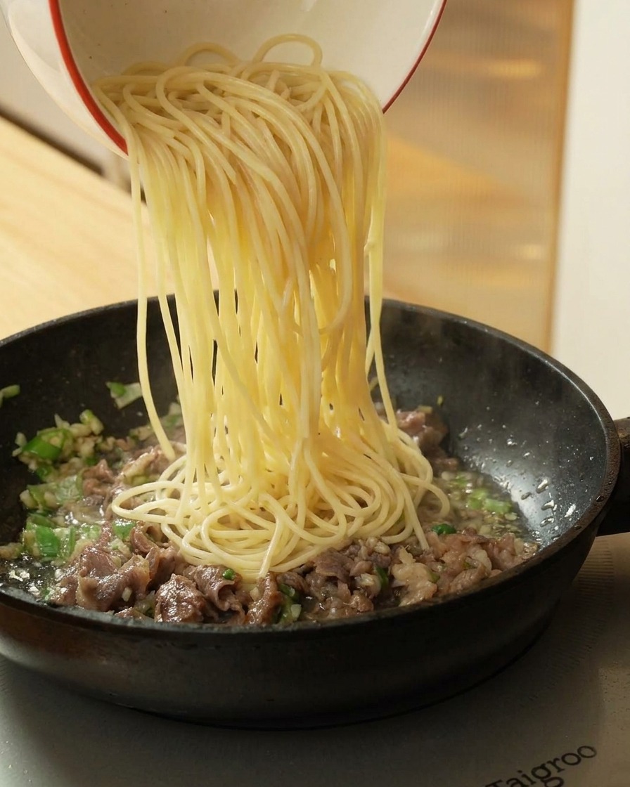 Versare gli spaghetti cotti nella padella con il manzo rosolato.