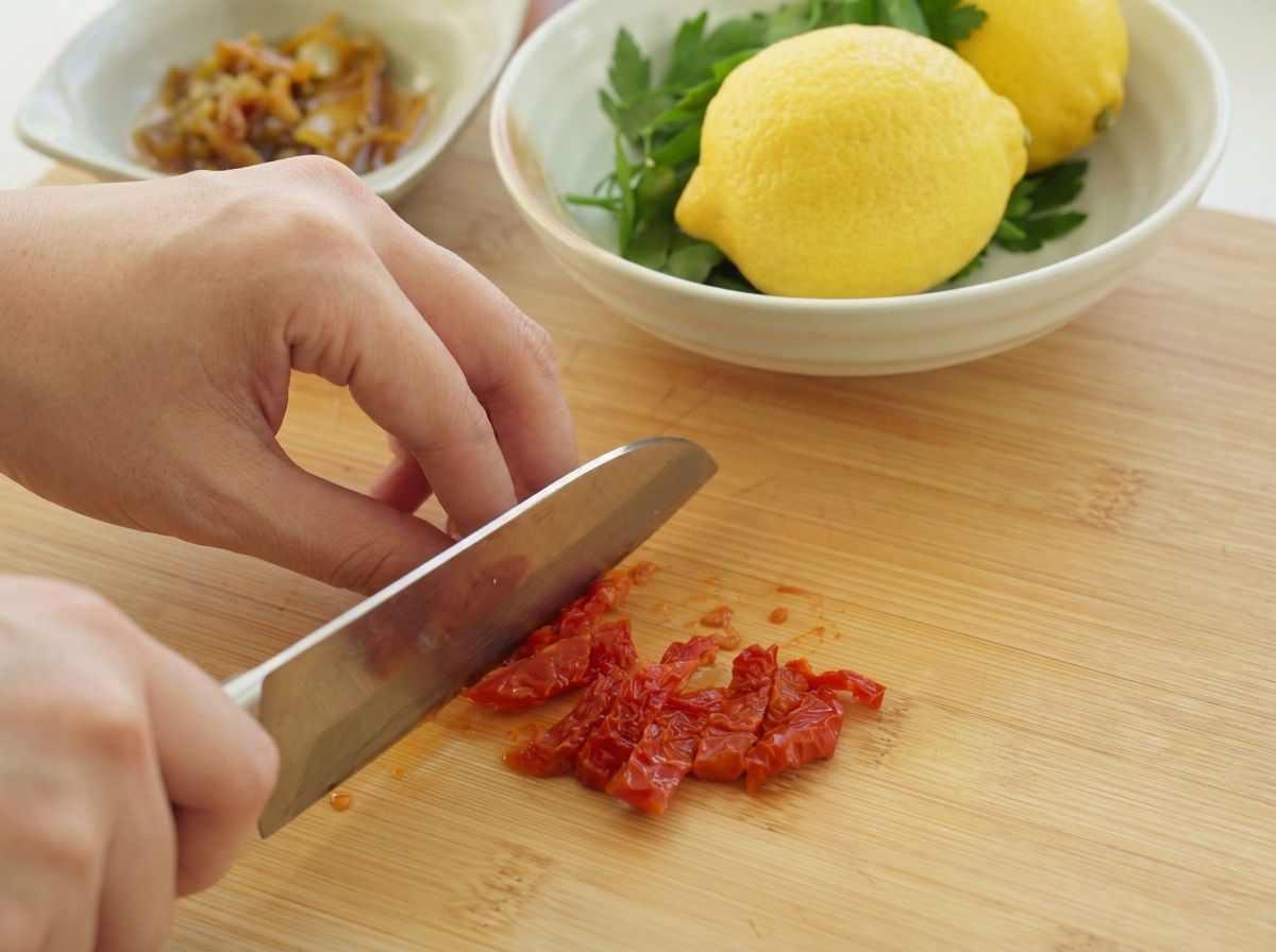 Sminuzzare finemente i pomodori secchi rosso intenso su un tagliere di legno con un coltello da chef.