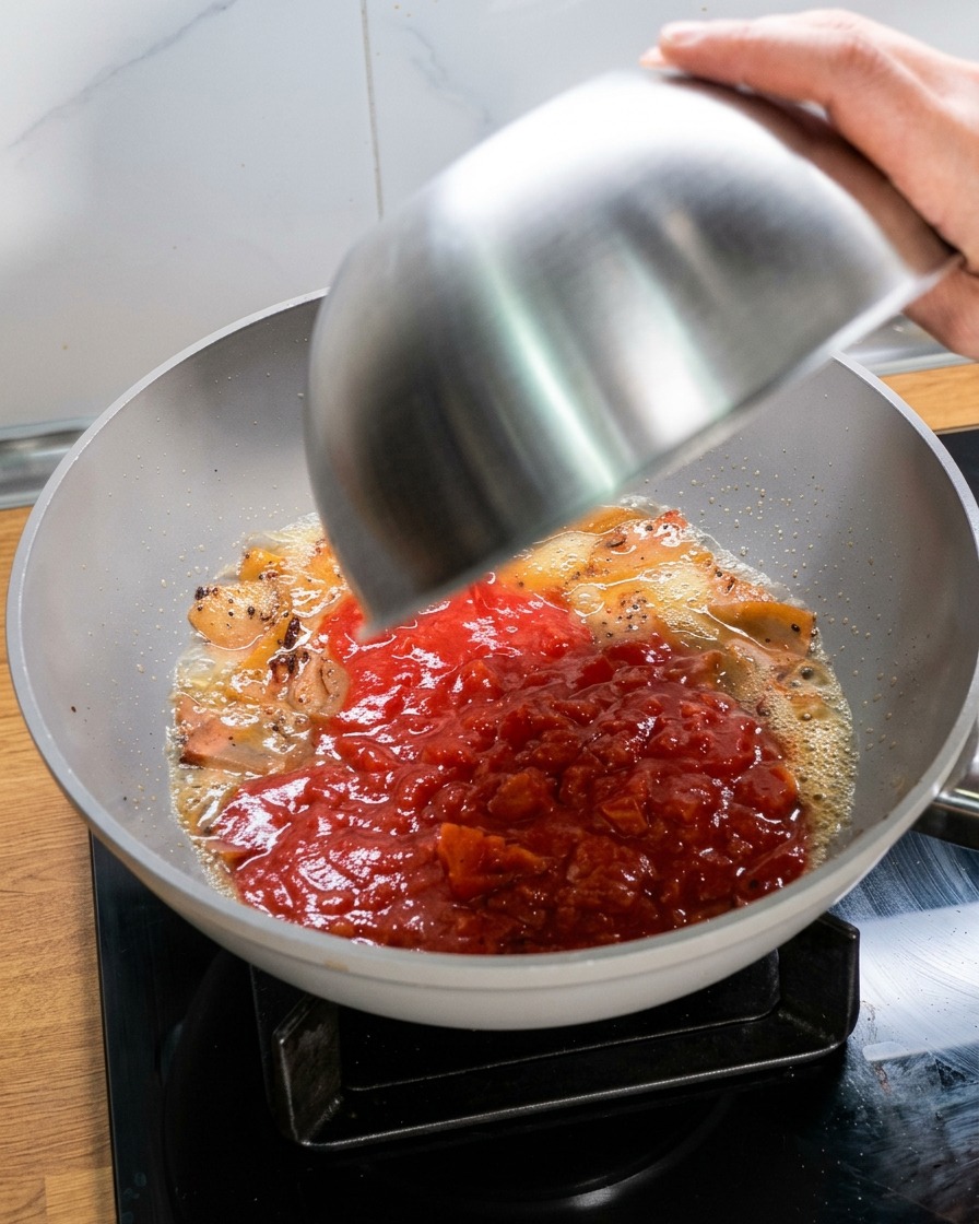 Versare una ciotola di pomodori schiacciati in una padella con il guanciale e il fondo di cottura.
