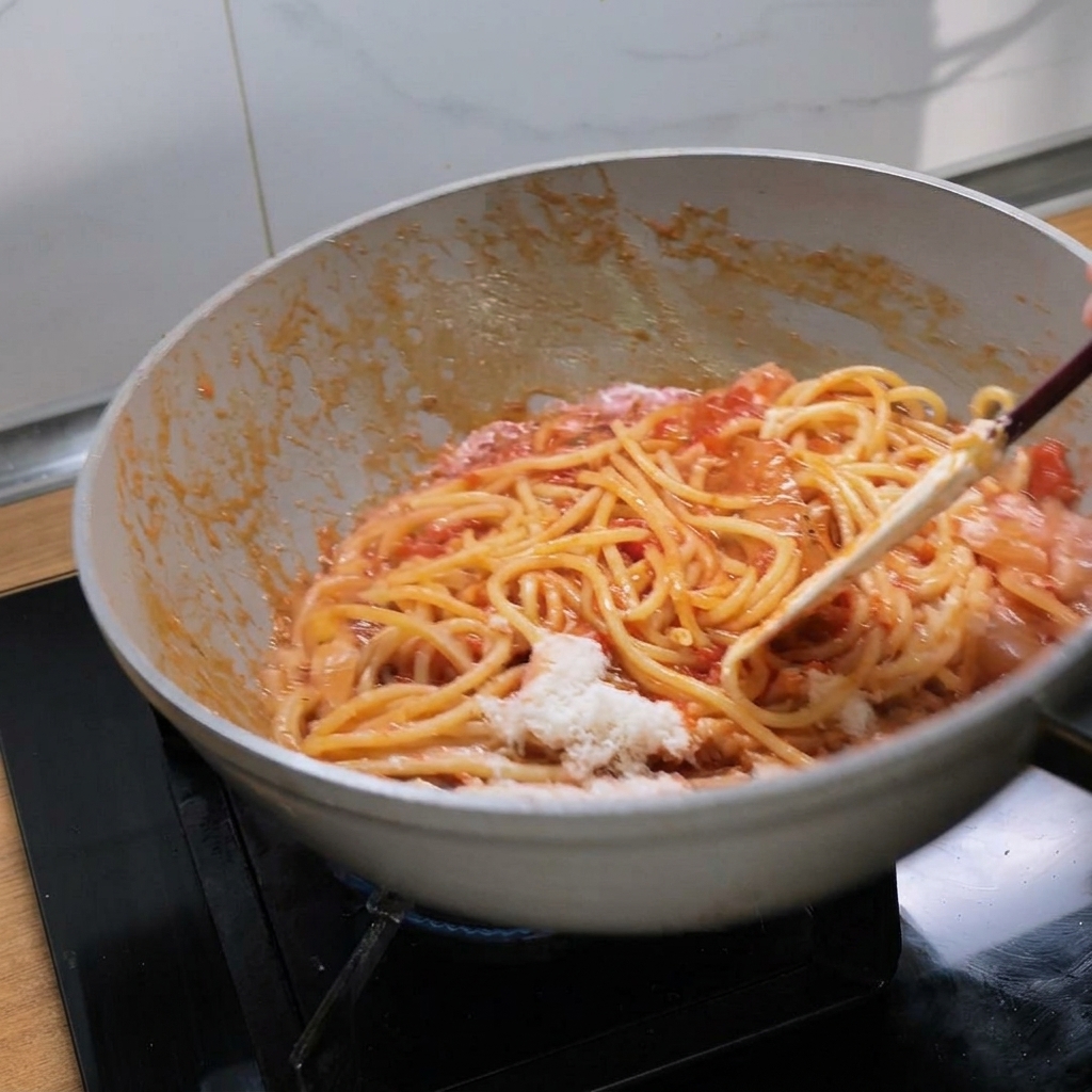 Saltare i bucatini con il sugo di pomodoro e il formaggio fuso in una padella bianca.