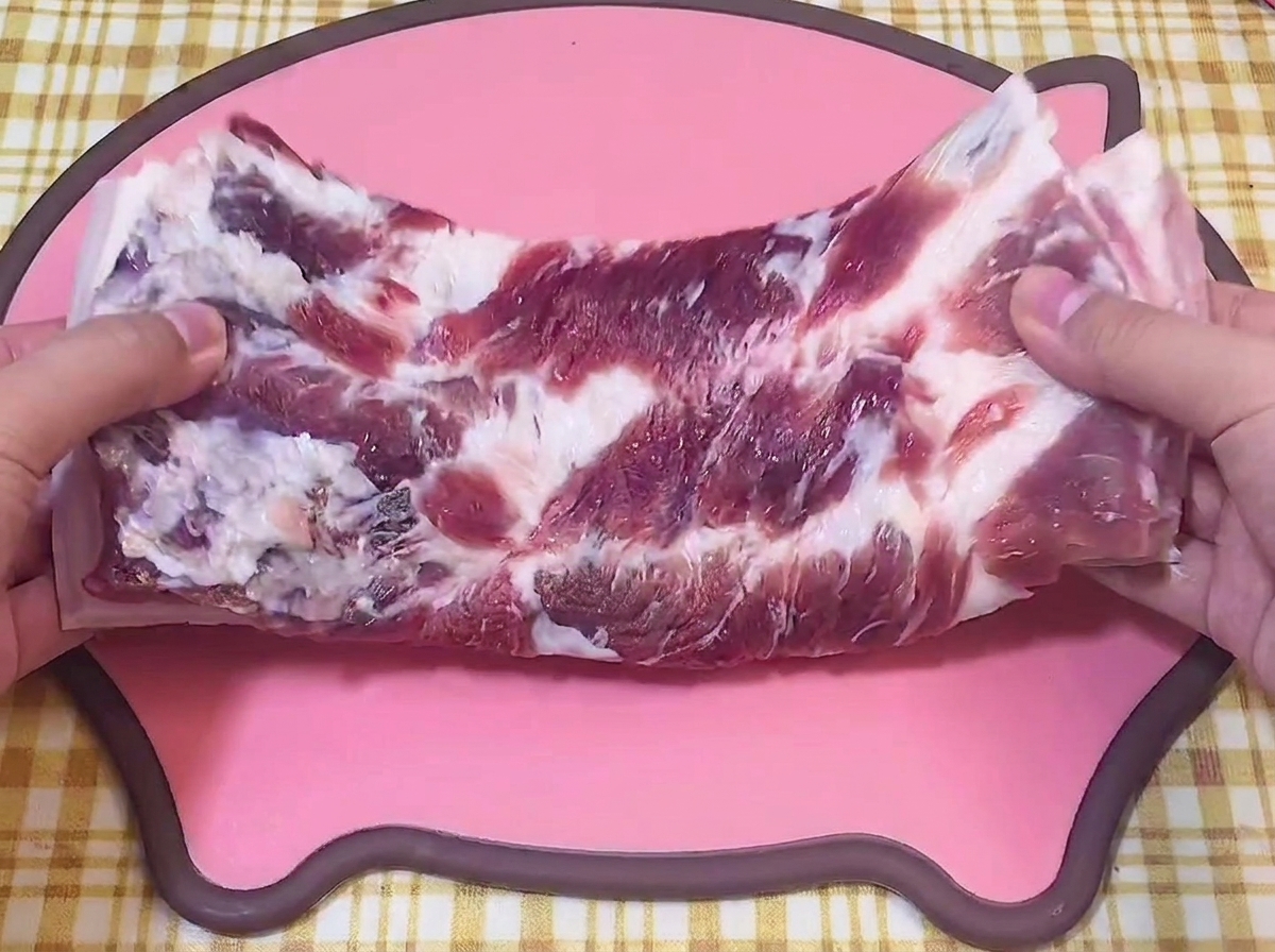 Mani che tengono un pezzo di pancetta di maiale cruda su un tagliere rosa a forma di maialino.