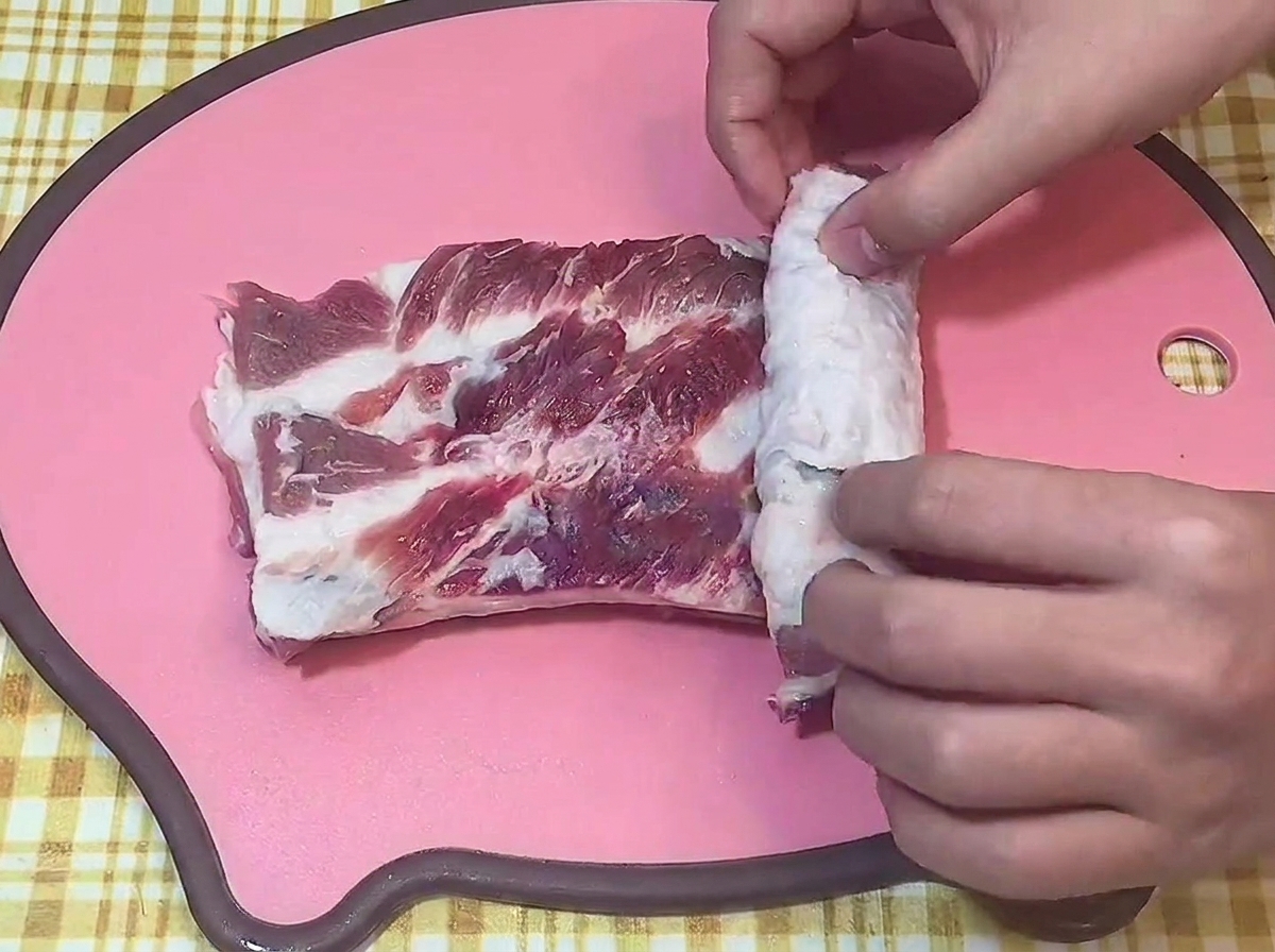 Mani che arrotolano strettamente la pancetta di maiale cruda su un tagliere.