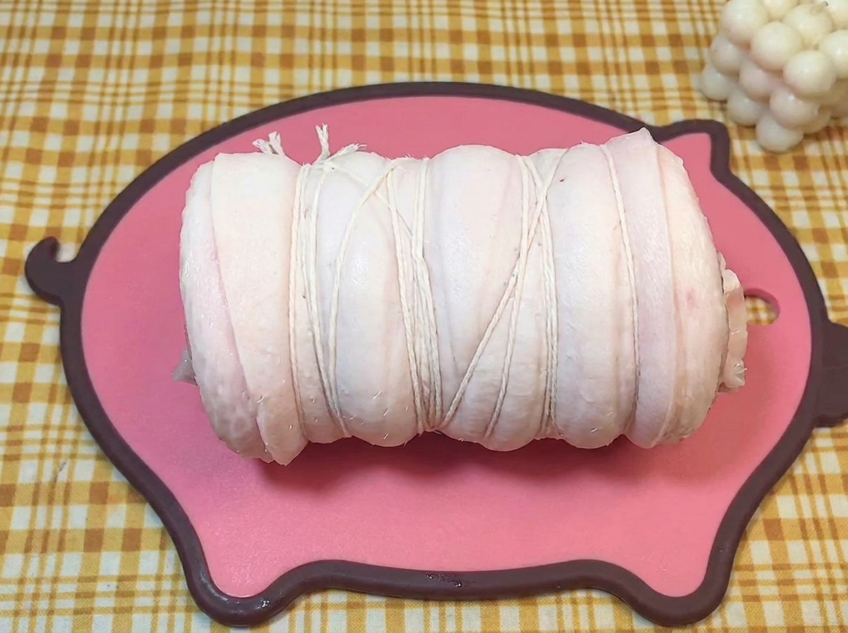 Un cilindro di pancetta di maiale cruda legato saldamente con spago da cucina bianco.