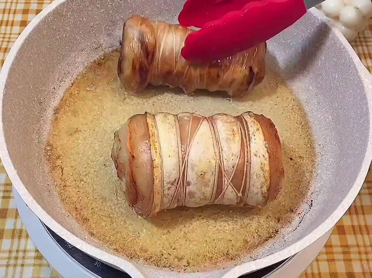 Due rotoli di maiale legati con una crosticina dorata e croccante in una padella.