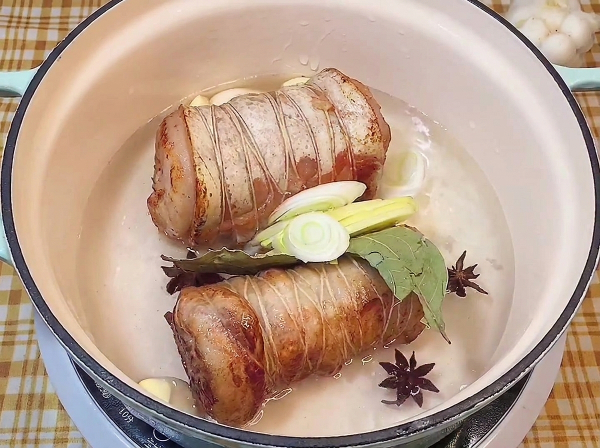 Rotoli di maiale rosolati in una pentola con liquidi, anice stellato, alloro, aglio e porri freschi.