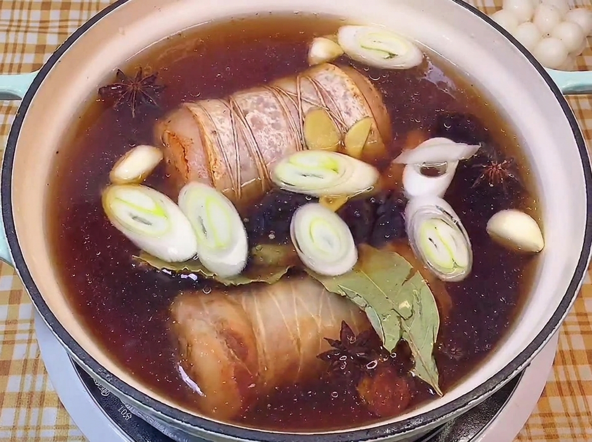 Pancetta arrotolata che sobbolle in un brodo scuro di salsa di soia con porri, aglio e anice stellato.