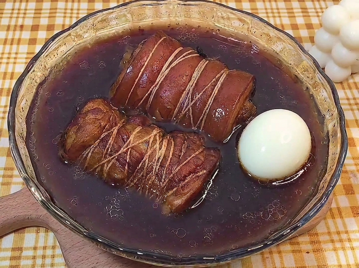 Due rotoli di chashu e un uovo sodo intero in una ciotola di vetro con liquido di brasatura scuro.