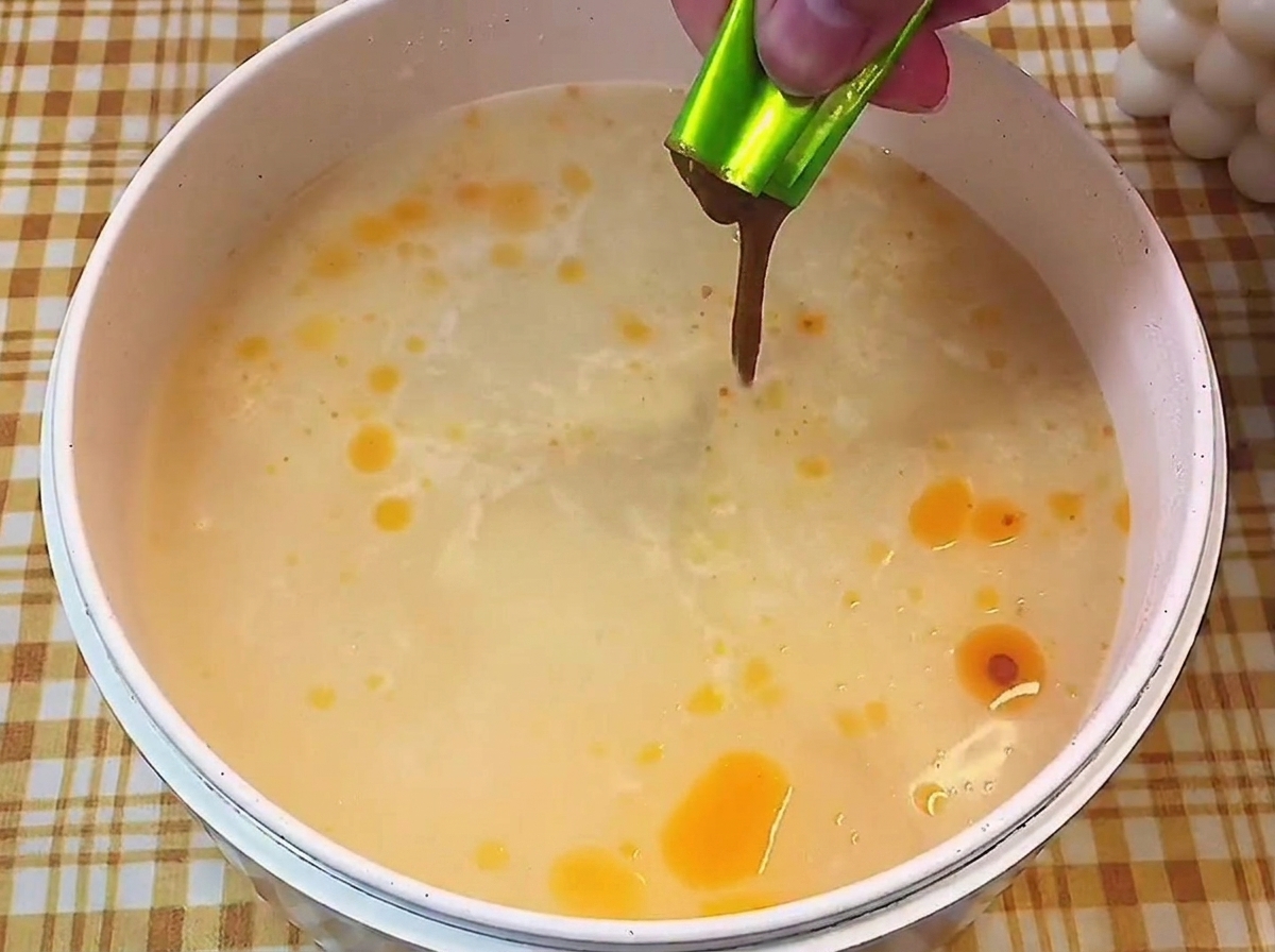 Mano che versa il condimento liquido concentrato in una pentola con brodo chiaro e fumante.