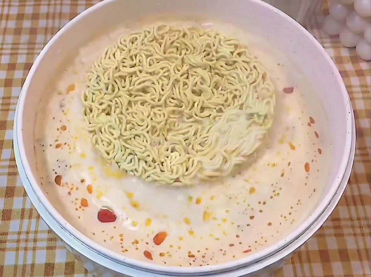 Blocco di noodles istantanei che galleggia in una pentola bianca con brodo insaporito.