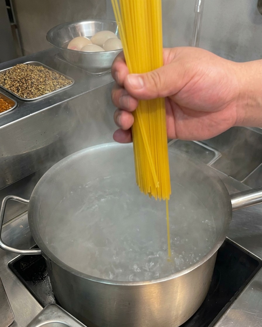 Una mano che inserisce spaghetti crudi in una pentola di acqua in forte ebollizione.