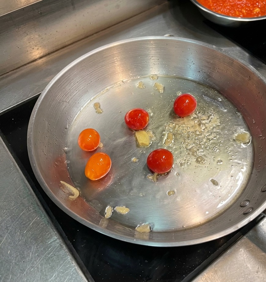Pomodorini interi che rosolano in olio caldo in unampia padella di acciaio inossidabile.